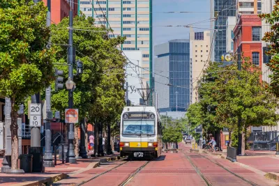 A white and yellow Dallas DART light rail train on track on street paved with red bricks in downtown Dallas, Texas.