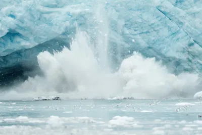 An iceberg from a glacier falls into an ocean.