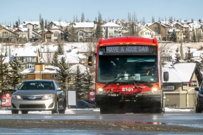 Red transit bus next to silver car on wet street.