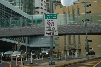 Sign for congestion pricing in front of an elevated pedestrian walkway with cars lined up underneath in New York City.