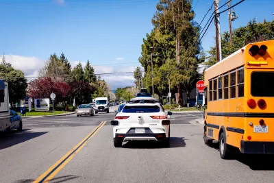 White Waymo self-driving car next to yellow school bus on street in Mountain View, California.