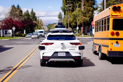 White Waymo car driving next to yellow school bus.