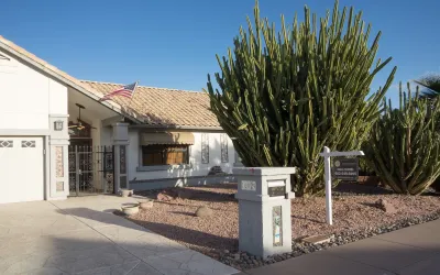 One-story beige home with large cactus in front yard with For Sale sign near sidewalk in Phoenix, Arizona.