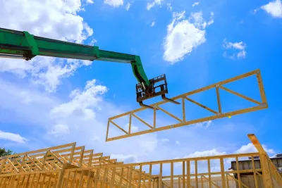 A green forklift holds up the scaffolding of a wall for a single-family home.