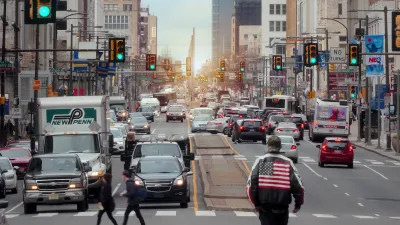 Traffic on street in Philadelphia, Pennsylvania with man wearing jacket with American flag on back in foreground.