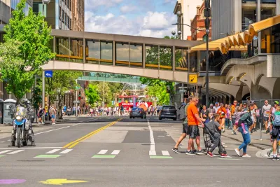 People walking across crosswalk in downtown Spokane, Washington with enclosed glass skyway connecting two buildings in background.