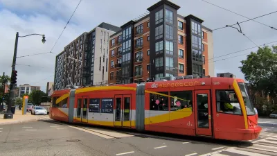 Red and yellow DC streetcar with multistory apartment building in background.
