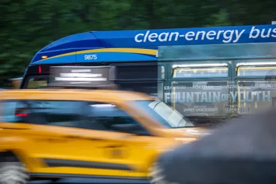 Blue :clean energy" bus blurred passing on city street.