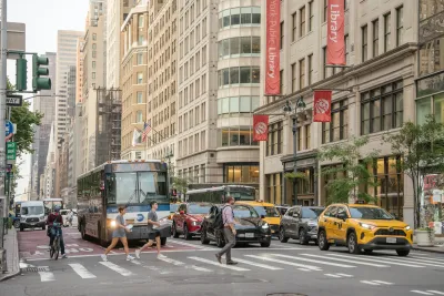 Pedestrians crossing New York City crossalk in front of bus and cars.