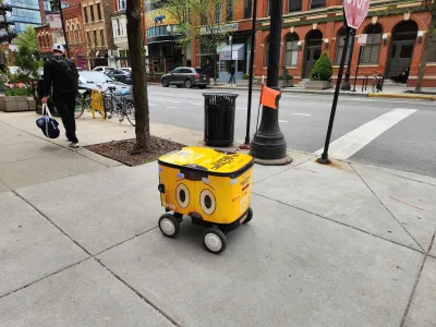 Yellow food delivery robot with cartoonish eyes on side rolling down sidewalk in Chicago, Illinois.