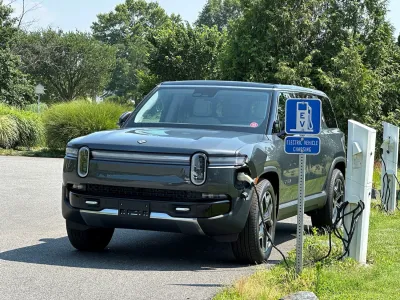 Dark grey Rivian truck plugged into roadside EV charging station.