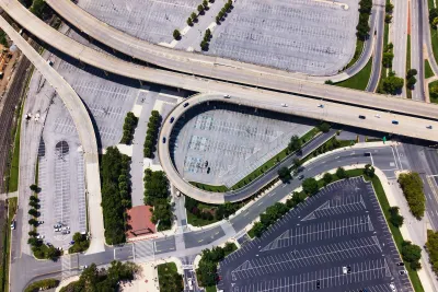 Aerial of wide freeway overpasses over large mostly vacant asphalt parking lots.