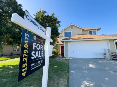 Close-up on For Sale sign in front of yellow house with white garage door.
