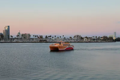 Yellow and red water taxi in Long Beach, California with tall palm trees on beach in background at sunset.
