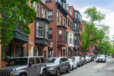 Line of cars parked curbside next to three-story brick homes with bay windows in Boston, Massachusetts.
