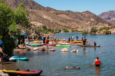People swimming near shore with parked kayaks on Colorado River beach in Arizona.