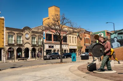 Street in downtown Green Bay, Wisconsin with statue of man beating large drum worn on his chest.