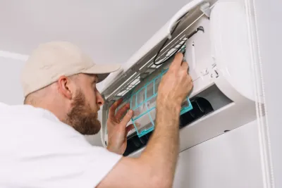 Man installing or repairing mini split air conditioning unit on white wall.