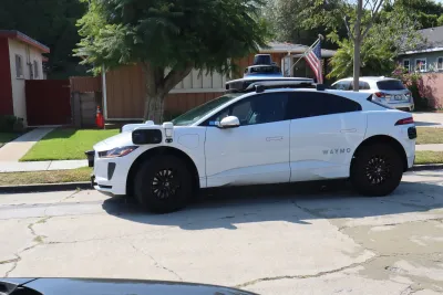 White Waymo autonomous car on small street in Los Angeles.