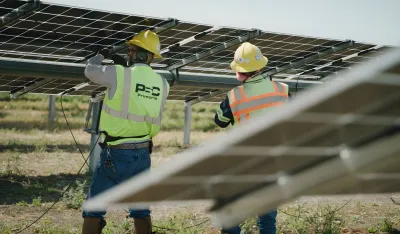 Technicians in green vests Installing Solar Panels at a Solar Farm.