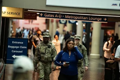 Woman in blue athletic clothes walks through DC Union Station with two National Guardsmen in uniform walking behind her.