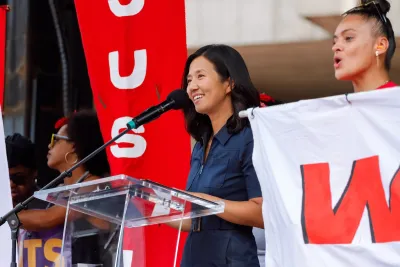 Boston Mayor Michelle Wu smiles behind a glass podium.