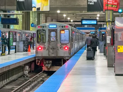 A  Chicago 'L' train stands ready at the station as travelers with luggage move about the platform.