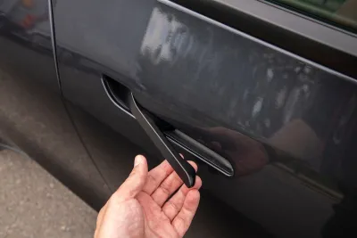 Close-up of hand pulling car door handle on dark grey Tesla.