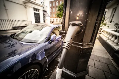 Close-up on utility pole with EV charger cable running out of it to dark-colored car plugged into it.
