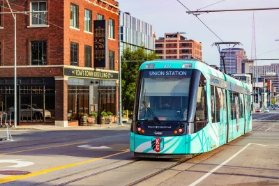 Green Kansas City streetcar driving down street next to brick building with vintage-style 'Tom's Town Distillery' sign.