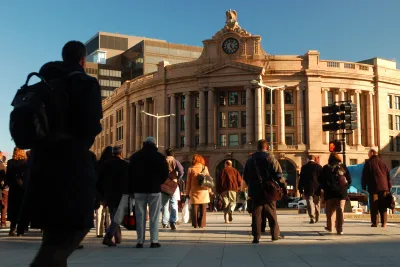 Neo-classical rounded South Station building with decorative clock on front and crowd walking in and out.