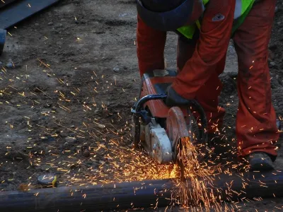 Construction worker uses a power saw to cut through metal.