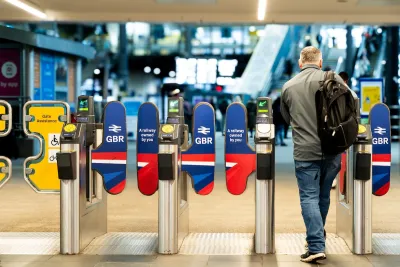 A rail passenger going through the ticket barrier at Leeds Train Station with the UK Government's re-nationalised rail company GBR signs and symbols displayed.