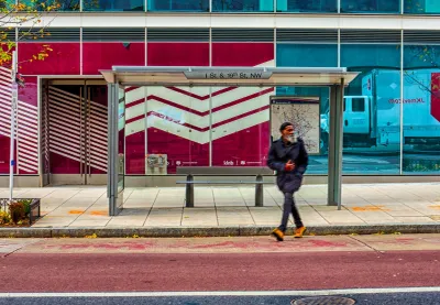 Man sitting at bus stop in Washington DC with red building wall in background.