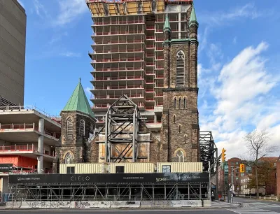 Multi-story apartment building under construction directly behind old stone church in Toronto, Canada.