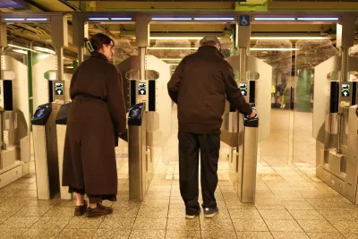 A man and a woman go through NYC's new turnstiles, which are tall, clear double doors.