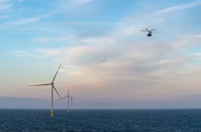 Row of offshore wind turbines in ocean with helicopter flying above.