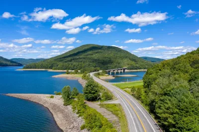 An aerial view of the Cannonsville Reservoir. A road splits in in two, and there are green mountains to the left, and in the background.