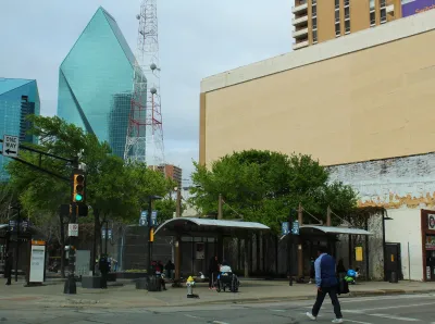 Bus stop with two shelters with benches with modern glass skyscraper with pointed pyramidal top in downtown Dallas, Texas.