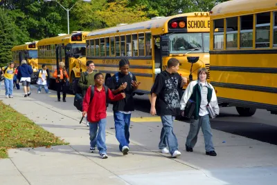 A group of children walk past yellow school buses on the way to school.