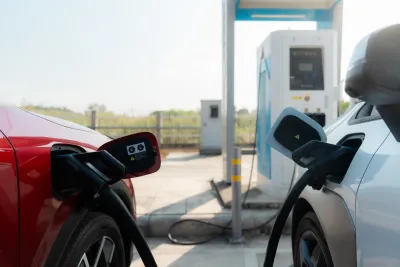 Close-up on red and white electric cars parked next to each other with charging cables plugged into them.