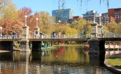 People crossing a bridge in Boston with fall leaves in the background.