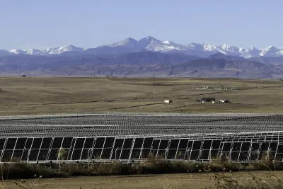 Solar panels n a field with Rocky Mountans visible in background.
