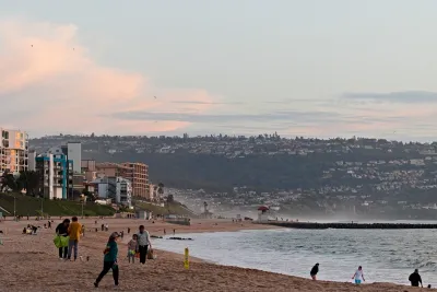 A crowd of people play in the sand at a California beach at sunset.