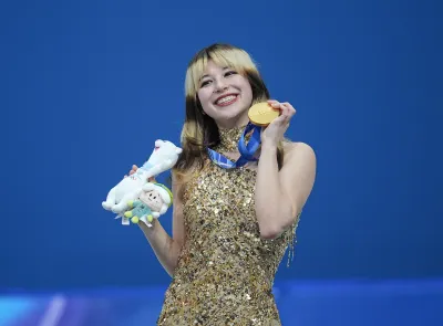 Figure skater Alysa Liu holds up her gold medal against blue backgrounf at the Milan-Cortino Olympics.