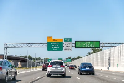 Sparse traffic on freeway with green and yellow signs for upcoming toll lanes.