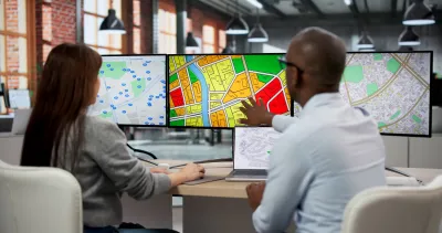 Two professionals sitting at desk with three-monitor computer showing zoning and other maps.