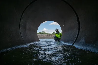 A person in a bright green jacket stares down a culvert, a pipe meant to divert rainwater from roads. 