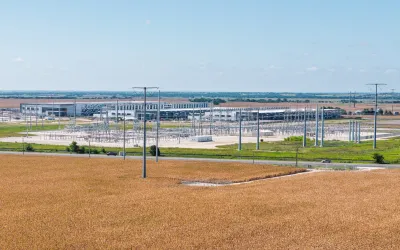 A power grid in Texas. There is brown dirt in the foreground, and trees in the background.