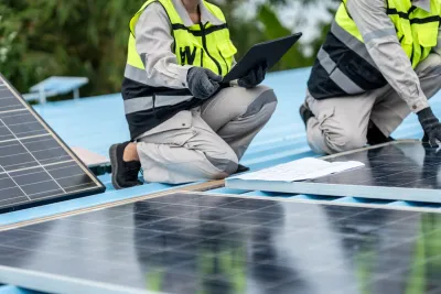 Two people in hi-vis vests install solar panels on a blue roof.